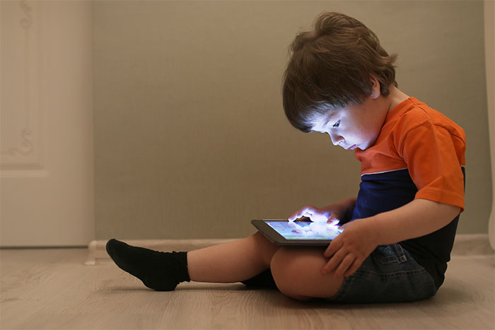Child focused on tablet in a dim room, illustrating concerns of iPad kids.