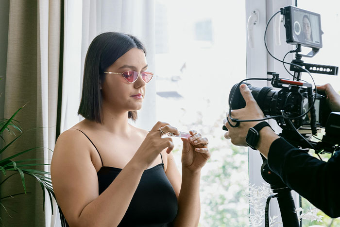 Woman with sunglasses records a video indoors, showcasing side hustle ideas.