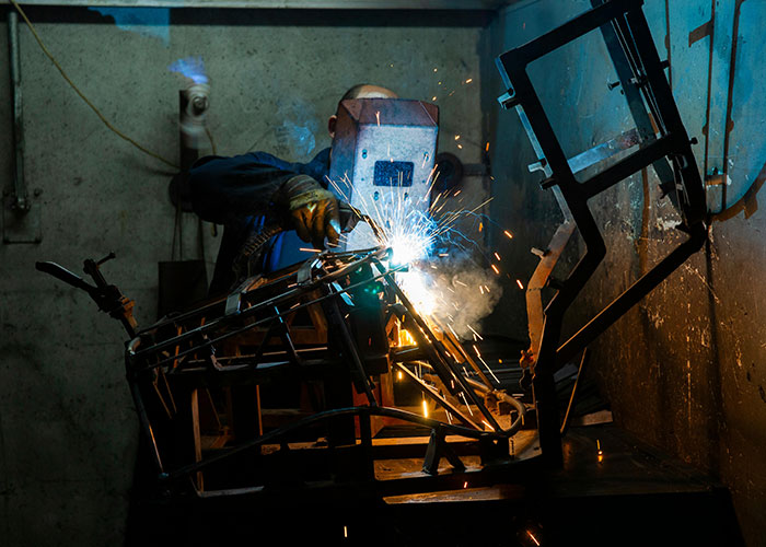 Welder at work in a dimly lit workshop, sparks flying as he welds metal structures.