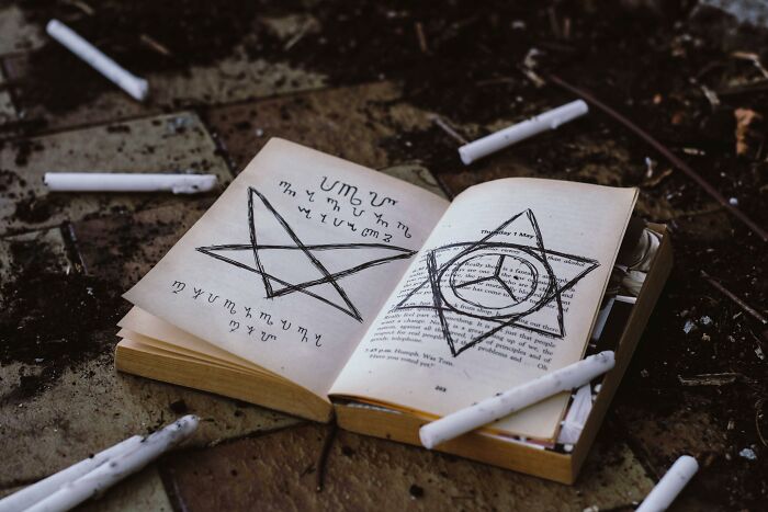 Open book on the ground with candles around, displaying mystical symbols; related to rumors theme.