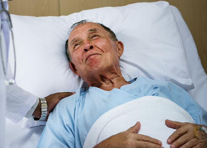Elderly patient in a hospital bed, appearing emotional, with a comforting hand on his shoulder, illustrating heartfelt last moments.