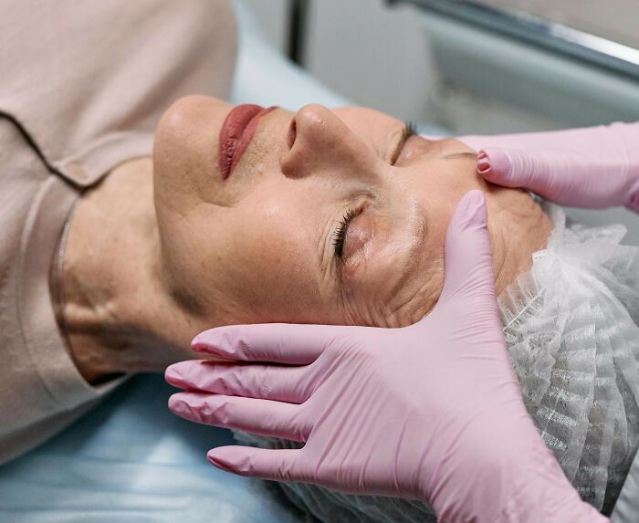 Person receiving a rare cosmetic procedure with gloved hands applying treatment to their face.