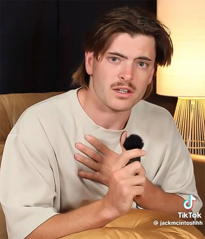 Podcaster with emotional expression, holding a microphone, referencing "Not All Men" discussion.