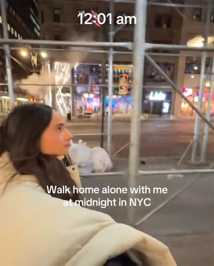 Woman walking in NYC at midnight, streets lit, scaffolding visible.