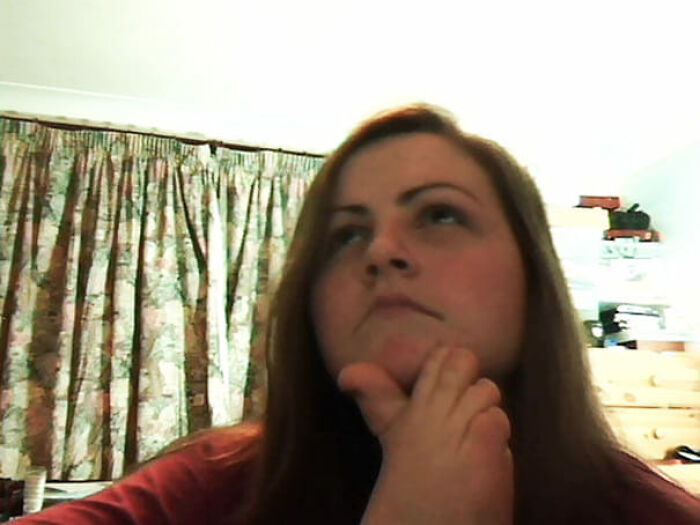 Person pondering with hand on chin, sitting in front of floral curtains; an example of weird images worth seeing.