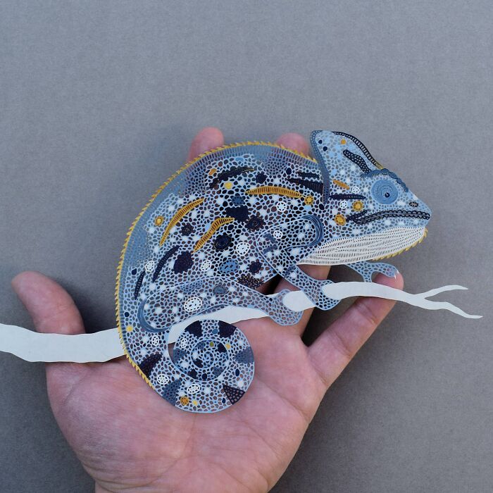 Intricate paper art design of a chameleon, held in a hand, showcasing nature-inspired patterns and details.