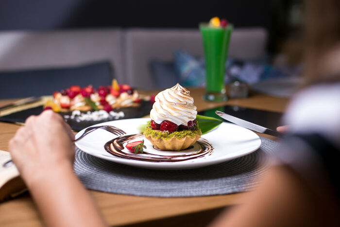 Person about to eat a dessert tart with whipped topping and berries on a plate, highlighting dessert experiences.