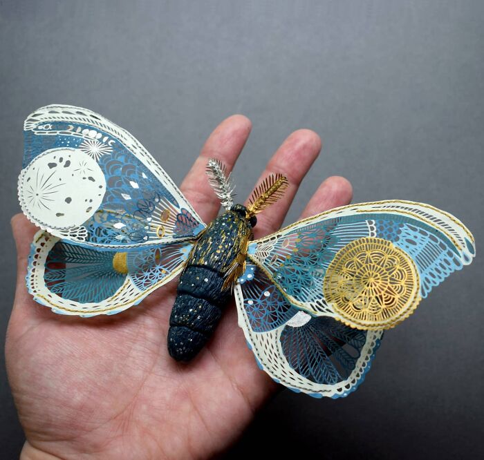 Intricate paper art design of a moth, showcasing nature-inspired details on a person's hand.