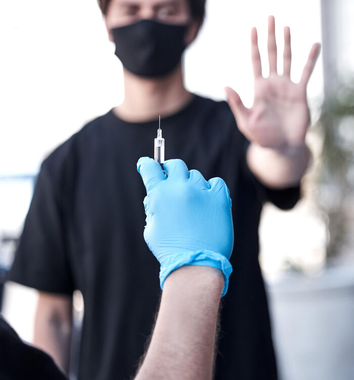 Person refusing syringe, wearing a black mask; illustrating non-physical qualities affecting attractiveness.