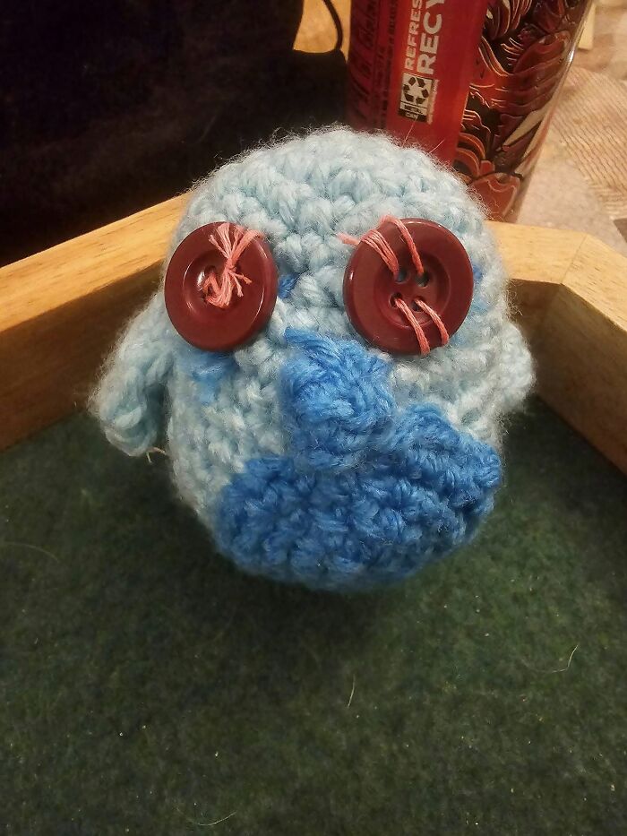 Crocheted creature with mismatched buttons for eyes, representing a humorous DIY craft project.
