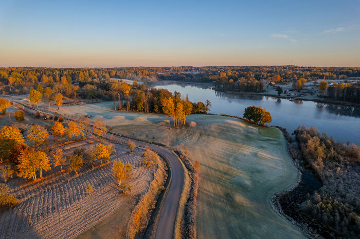 Aerial view of Lithuania's picturesque landscape with a river, autumn trees, and a winding road.