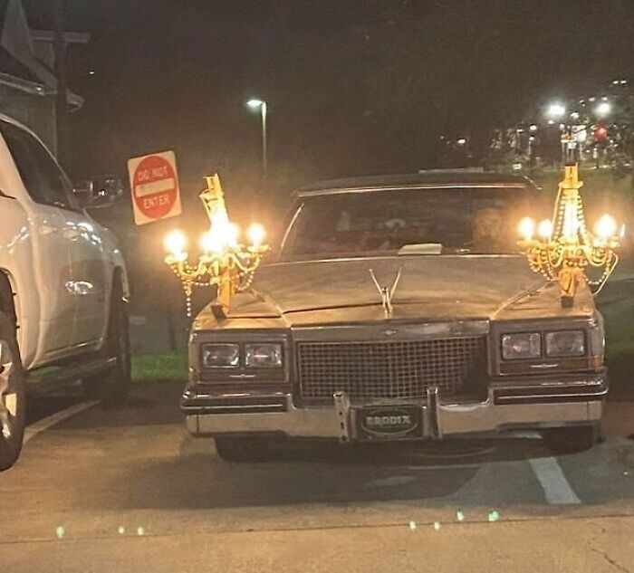 Vintage car adorned with candlelit chandeliers parked at night, showcasing unique cultural flair.