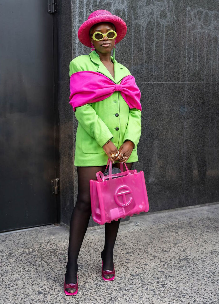 Fashion risk with bright green blazer, pink accessories, and black tights on a city sidewalk.