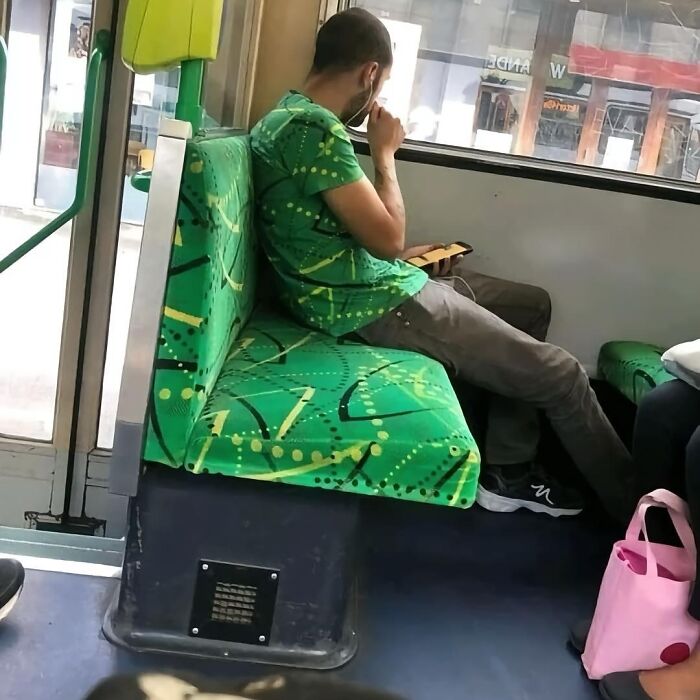 Man in a green patterned shirt sitting on a bus, looking at his phone, showcasing cultural street style.