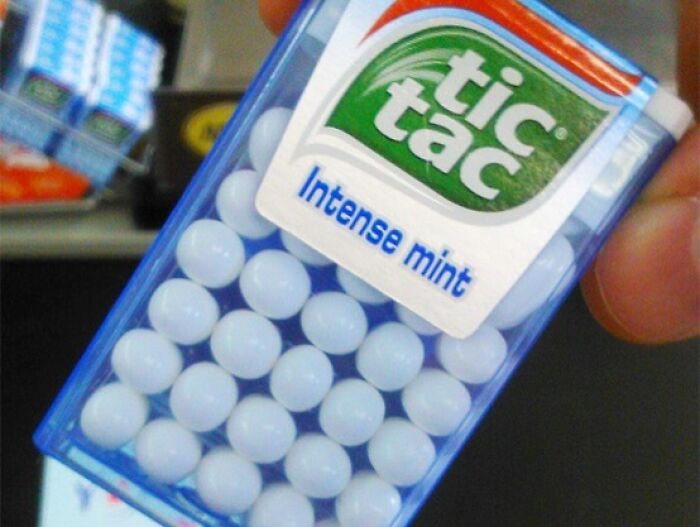A pack of round white Tic Tac mints labeled "Intense Mint" held in a hand, emphasizing an interesting image.