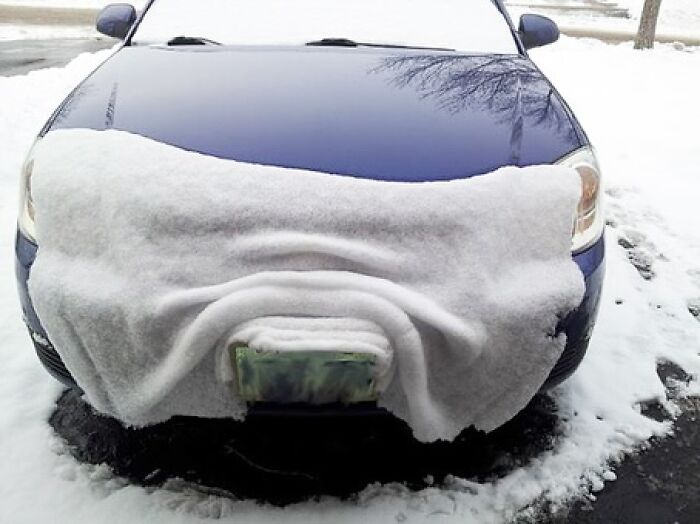 A car's front covered in snow, resembling a frowning face; interesting image capturing winter humor.