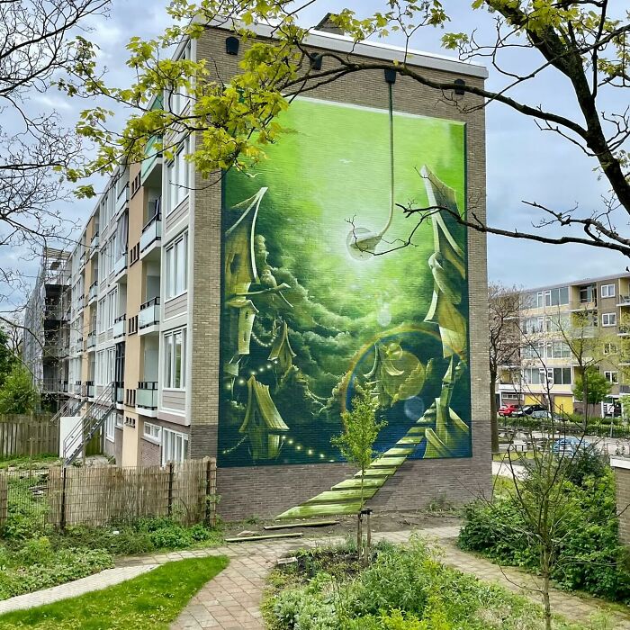 Mural by Jan Is De Man depicting a green surreal hyperrealistic illusion on a city building wall.