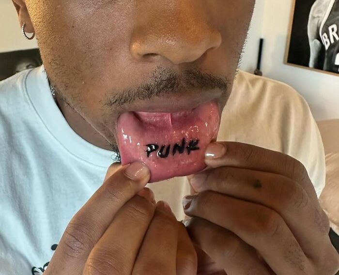 Man showing a tattoo on the inside of his lip with the word "punk," highlighting recent fashion trends people hate.