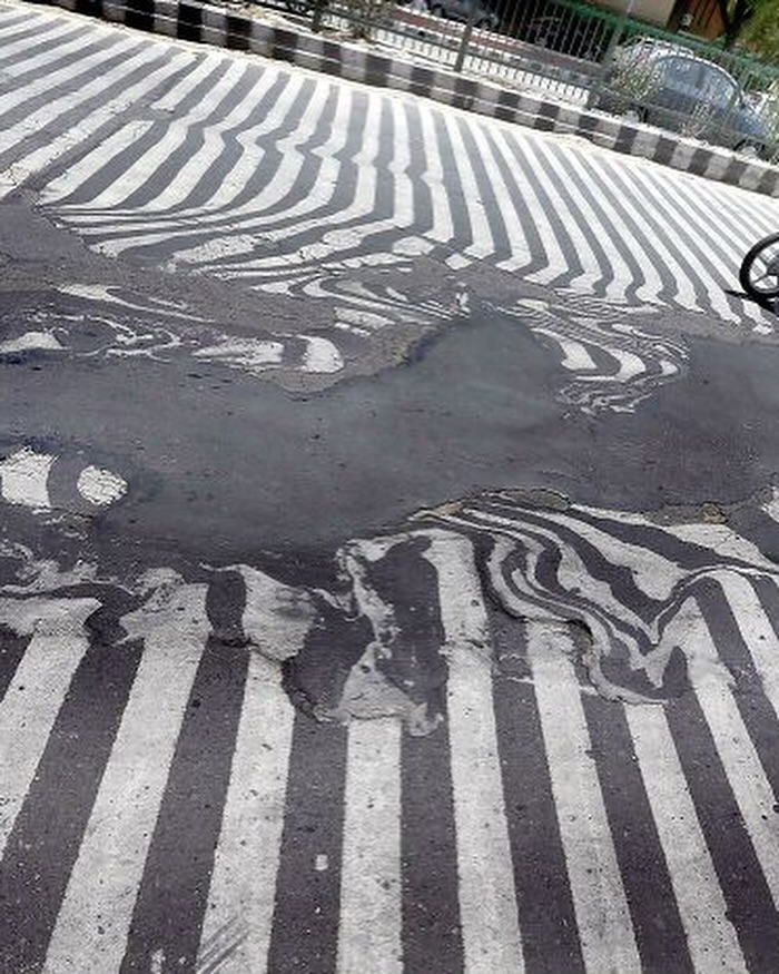 A zebra crossing with distorted lines on a busy road, part of an interesting image collection on Cultureavenue.