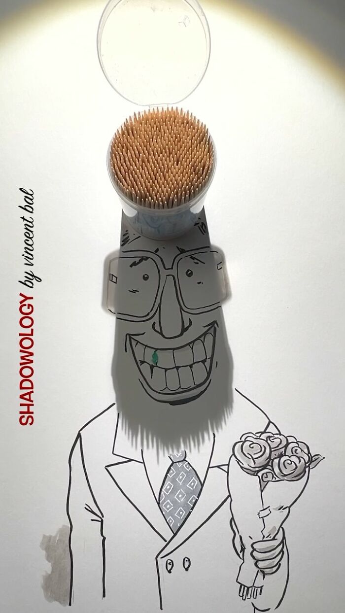 Artist transforms shadow of toothpick container into a smiling face illustration holding flowers.