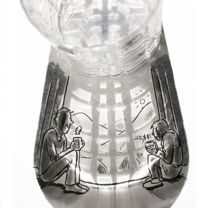 A glass casts a shadow transformed into an illustration of two people with mugs, gazing out a window at sunrise, by an artist.