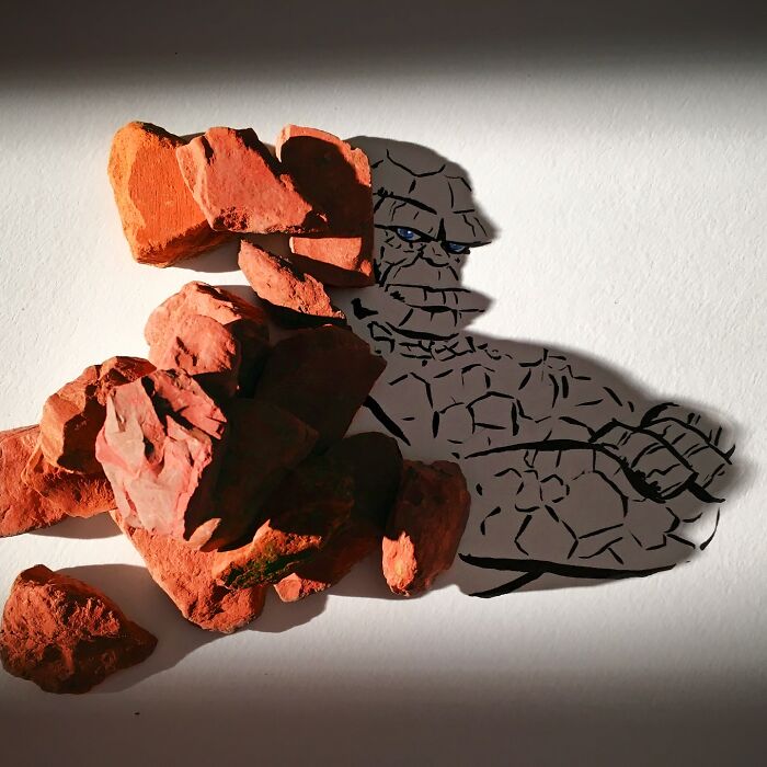 Artist uses shadow of rocks to create illustration of a stone figure on paper.
