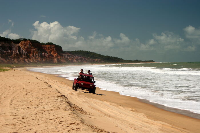 Retro Brazilian beach scene with a red jeep driving on sand by the ocean.