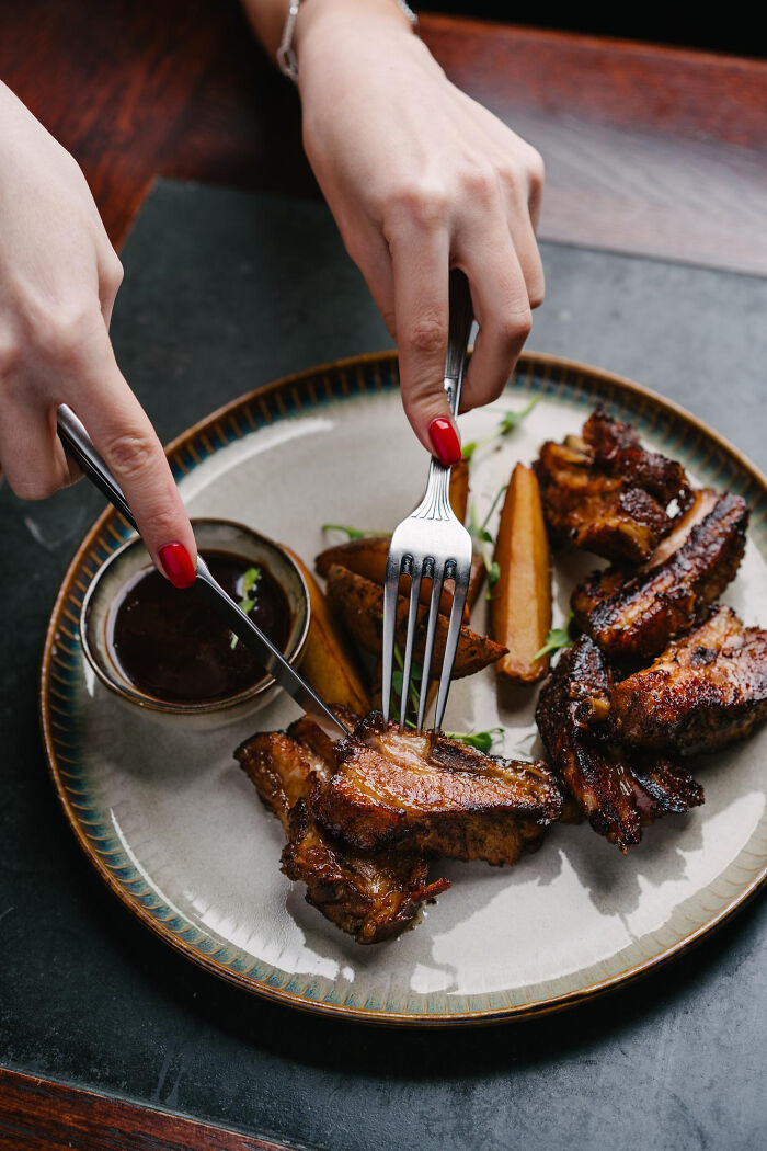 Cutlery cutting ribs, symbolizing unattractive eating habits, on a plate with dipping sauce.