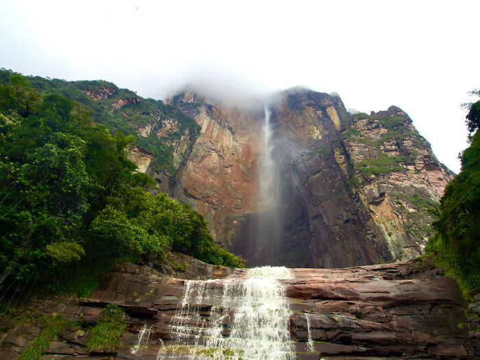 Waterfall cascading down a towering cliff, surrounded by lush greenery, showcasing a natural wonder.