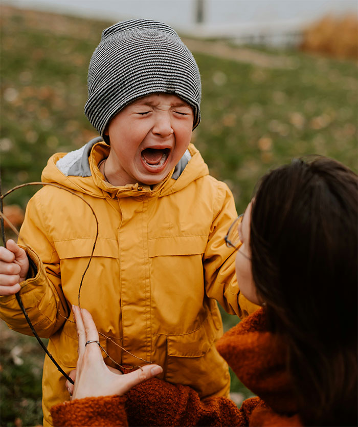 Child in a yellow jacket crying outdoors, a woman comforting them, illustrating concerns about "iPad kids.
