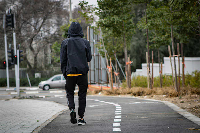 Teen in a black hoodie walking on a path, surrounded by trees, used to depict fake account creation scenario.