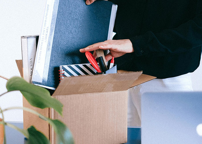 Person packing office supplies into a cardboard box, symbolizing a work-related change or revenge against a boss.