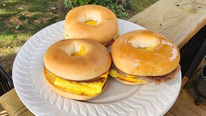 Bagels with egg and cheese on a white plate, set on a wooden outdoor table.