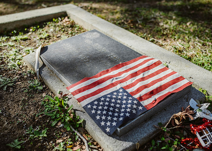 American flag draped over a tombstone, surrounded by autumn leaves and flowers, conveying a wholesome tribute.