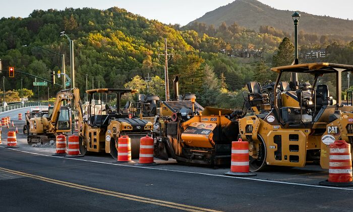 Construction vehicles lined up on the road, surrounded by orange cones, ready for essential repair work.