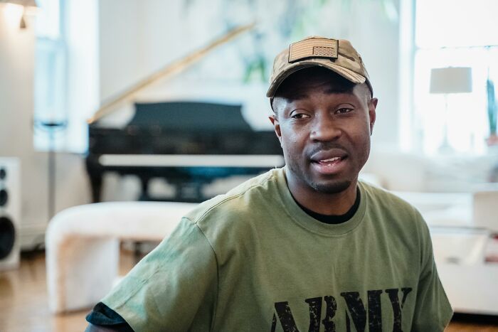 Man wearing an Army shirt and cap in a living room, highlighting deeply weird flags of people.