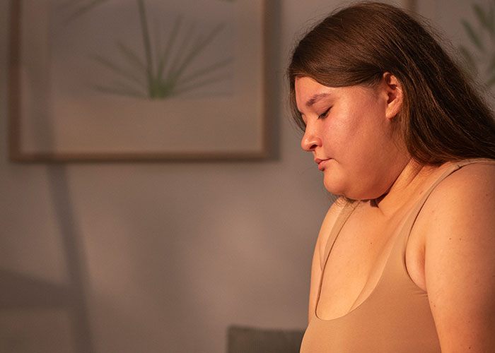 Person sitting indoors, deep in thought, exploring challenges of being overweight.