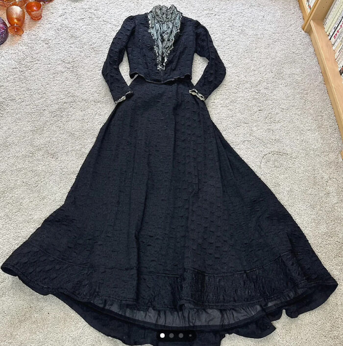 A vintage black dress with lace details found while thrifting, laid out on a carpeted floor.