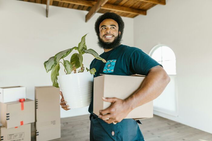 Man holding a plant and box, illustrating changing mindsets in a minimalist room.