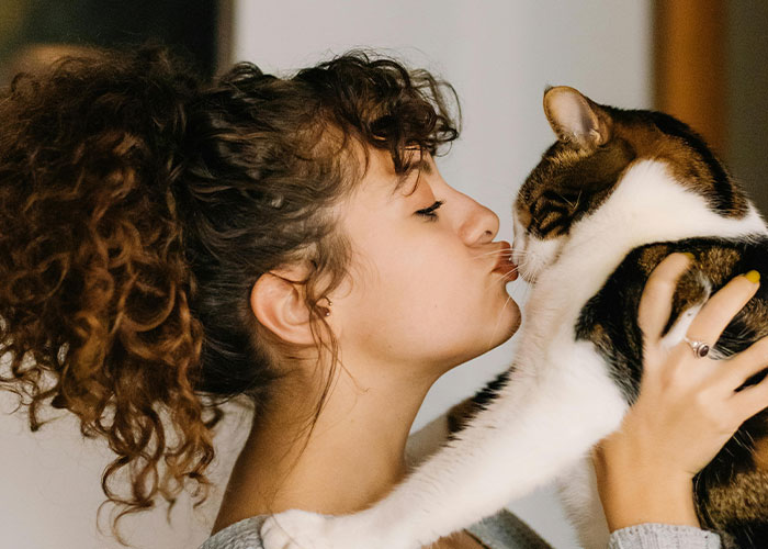 Woman kissing a cat, showing whimsical affection and joy.