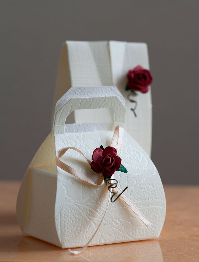 Elegant wedding favor box with a red rose and ribbon on a table.