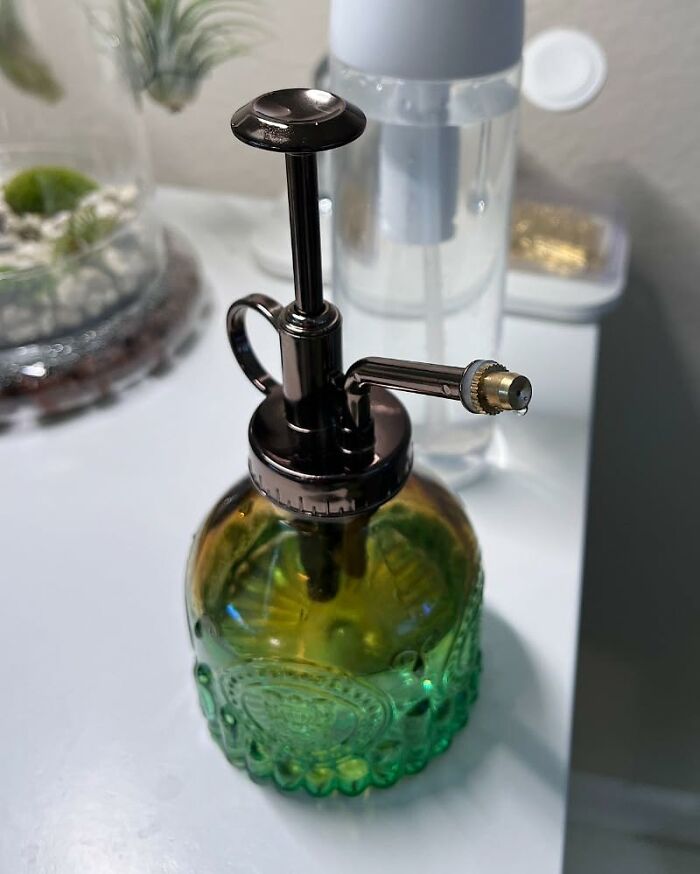 Indoor gardening essentials: a decorative green glass plant mister on a white surface, used for watering plants.