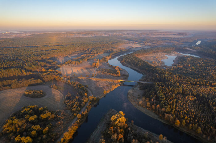 Aerial view of Lithuania's lush forests and winding rivers under a clear sky.
