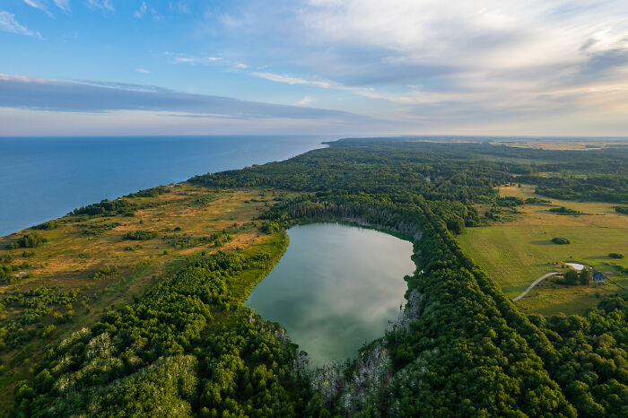 Bird’s-eye view of Lithuania with a serene lake surrounded by lush greenery and coastline.
