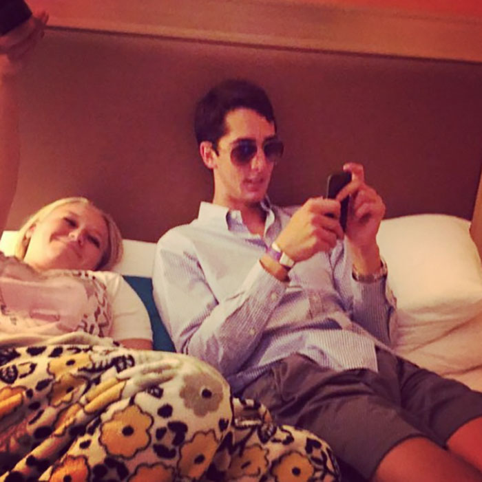 Young man in sunglasses using a phone, sitting on a bed beside a woman, related to terrifying backstories.