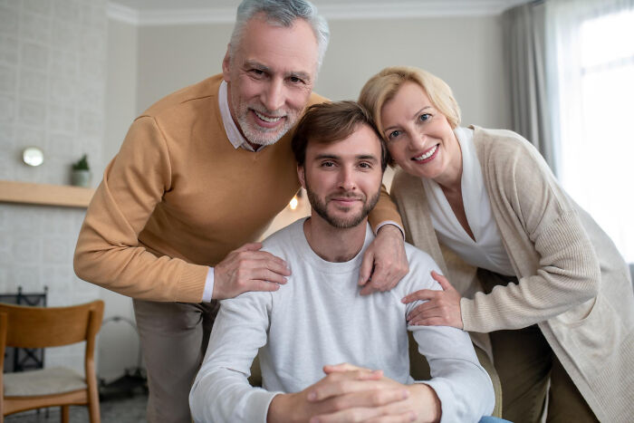 Middle-aged couple with adult son smiling, representing experiences people were raised to think were common.