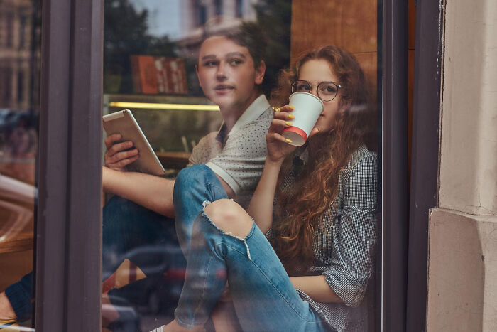 Two people sit by a window, one holding a tablet and the other drinking coffee, reflecting on rules made for one individual.