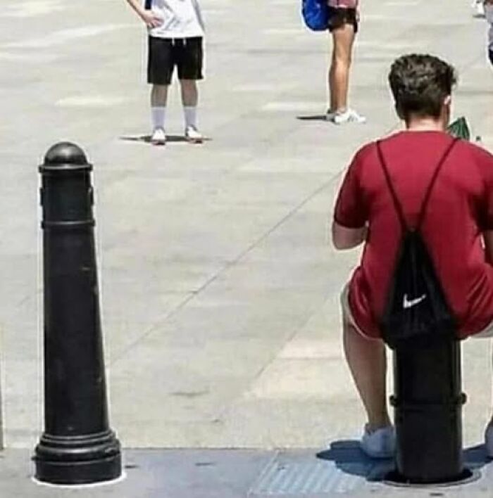 Person in red shirt sitting on a bollard in a public square, creating a weird image with others walking around.