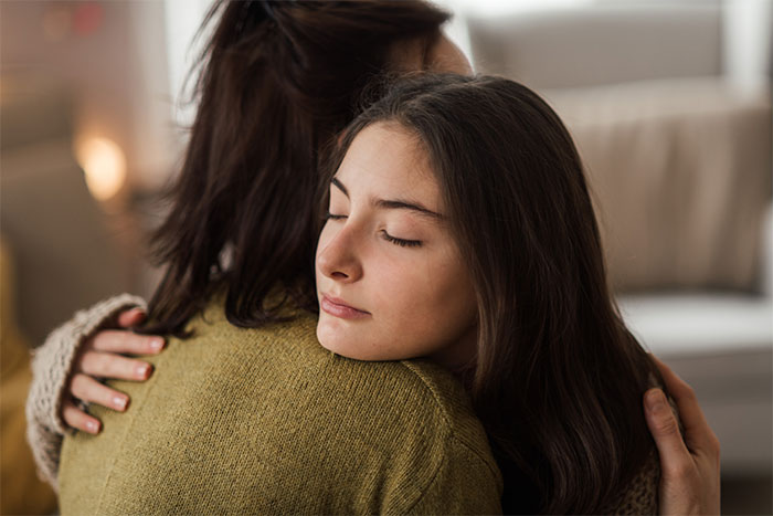 Teen girl hugging mother, eyes closed, highlighting babysitter volunteering tension.