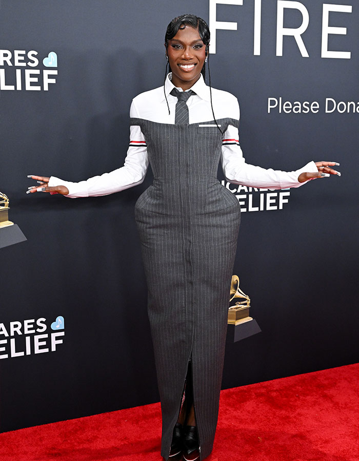 Person on red carpet at 2025 Grammys, in unique gray outfit with tie and white shirt, smiling and posing for photo.